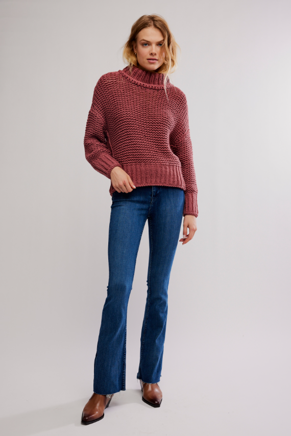 Woman wearing a rose cranberry colored chunky knit sweater with mock neck and dark jeans