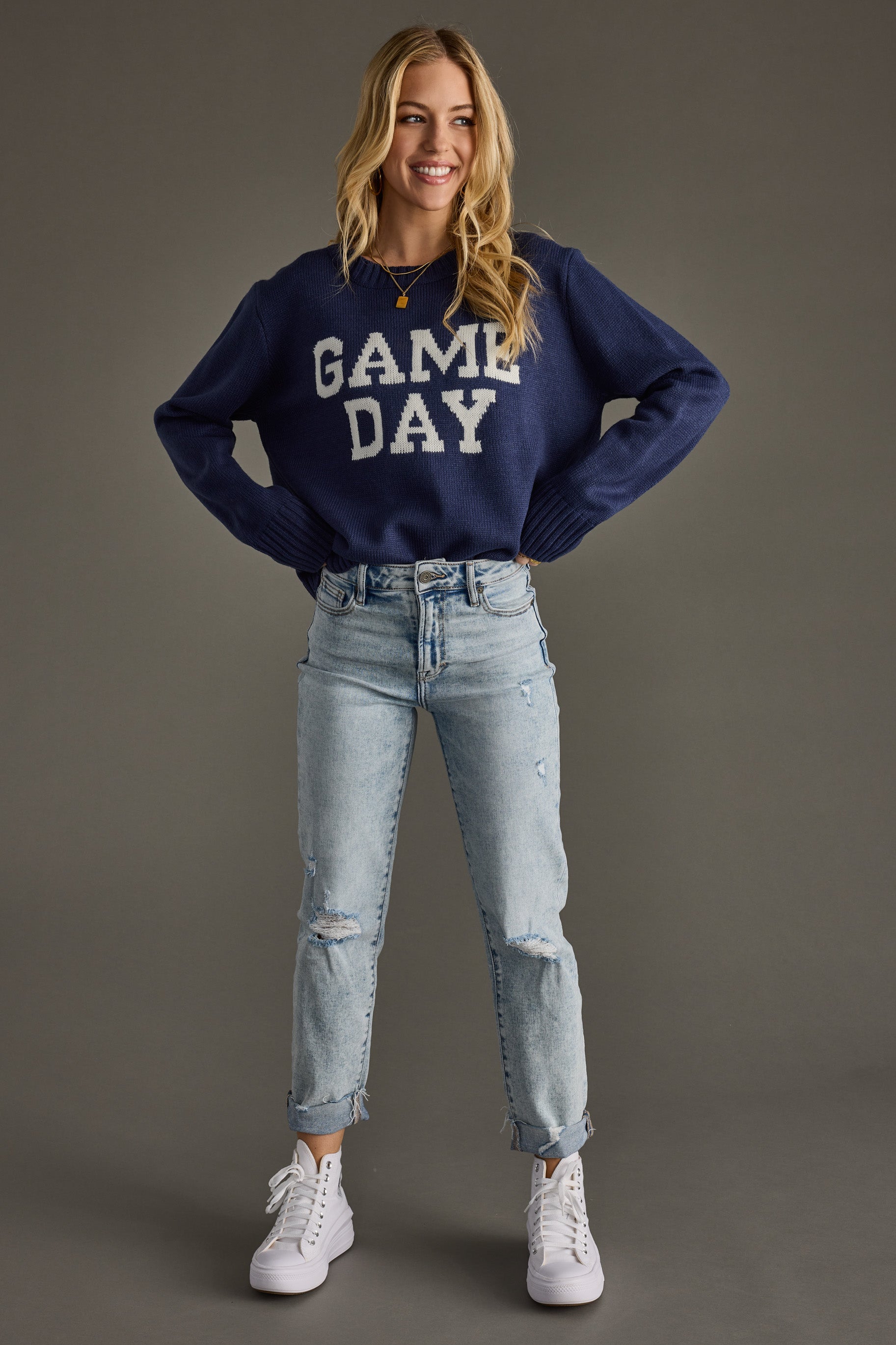 Woman wearing a navy 'GAME DAY' sweater with light blue jeans on a gray background