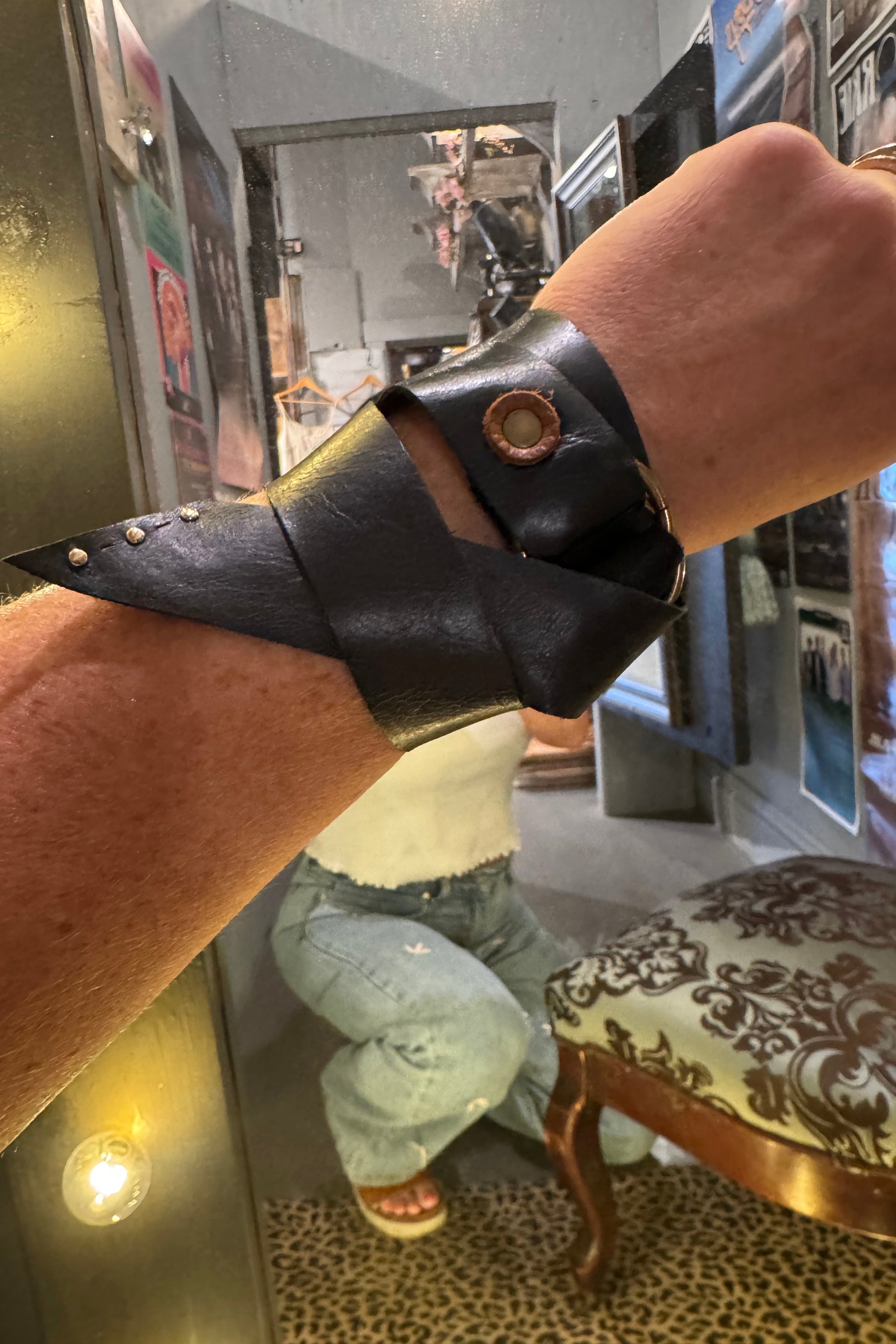 Person wearing a black leather wristband with a gold buckle on a reflective surface.