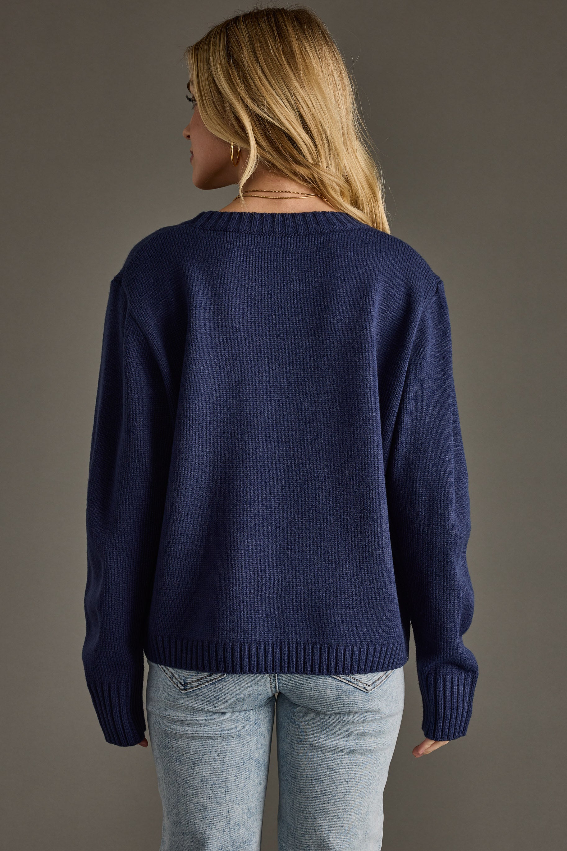 Person wearing a navy blue sweater and light blue jeans against a gray background