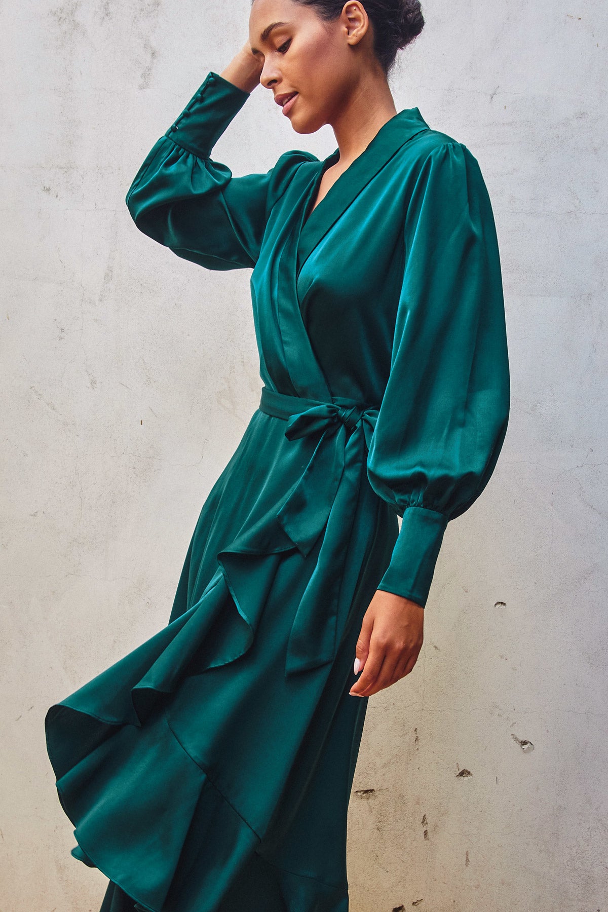 Model wearing a green satin holiday wrap dress with ruffles