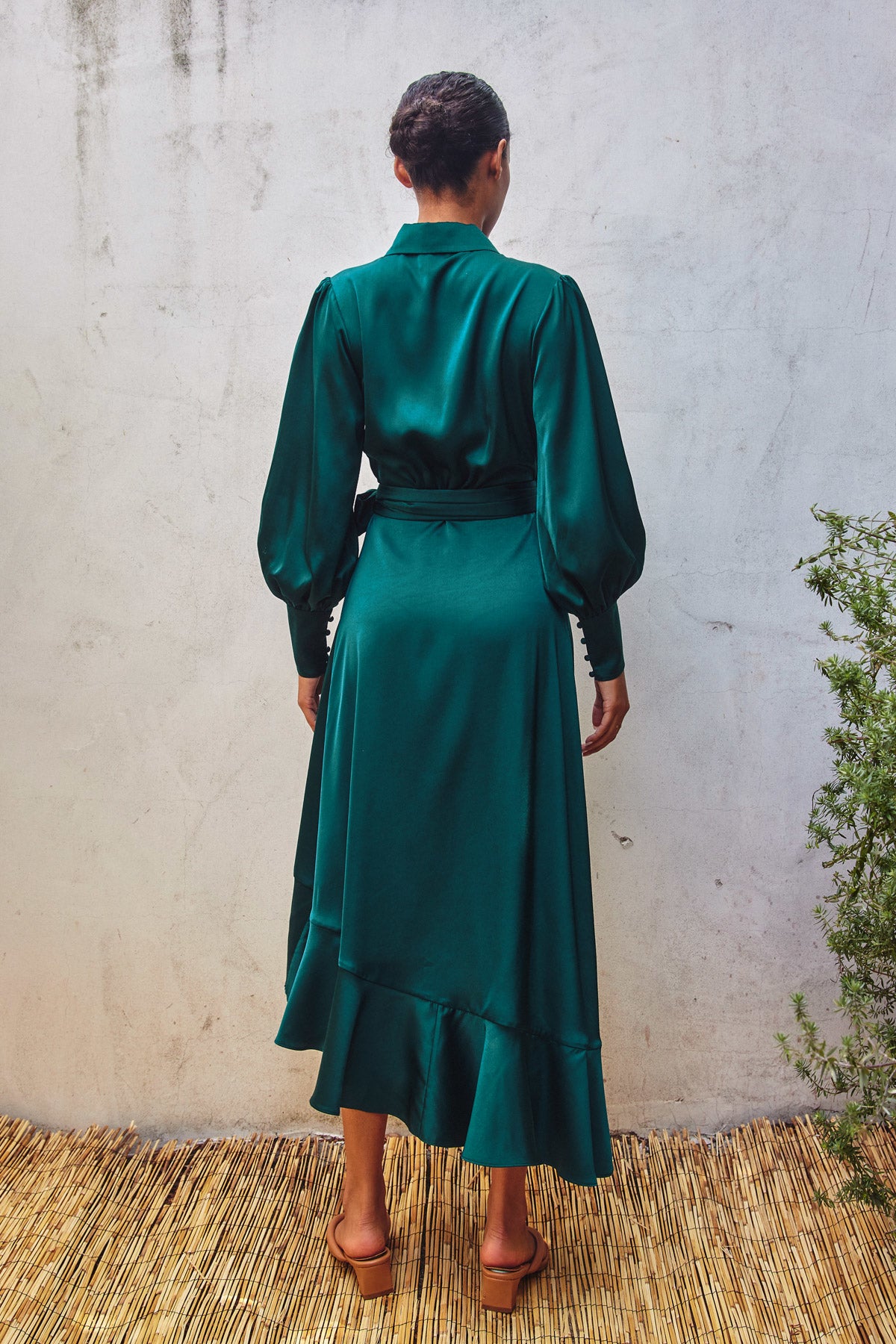 Model wearing a green satin holiday wrap dress with ruffles