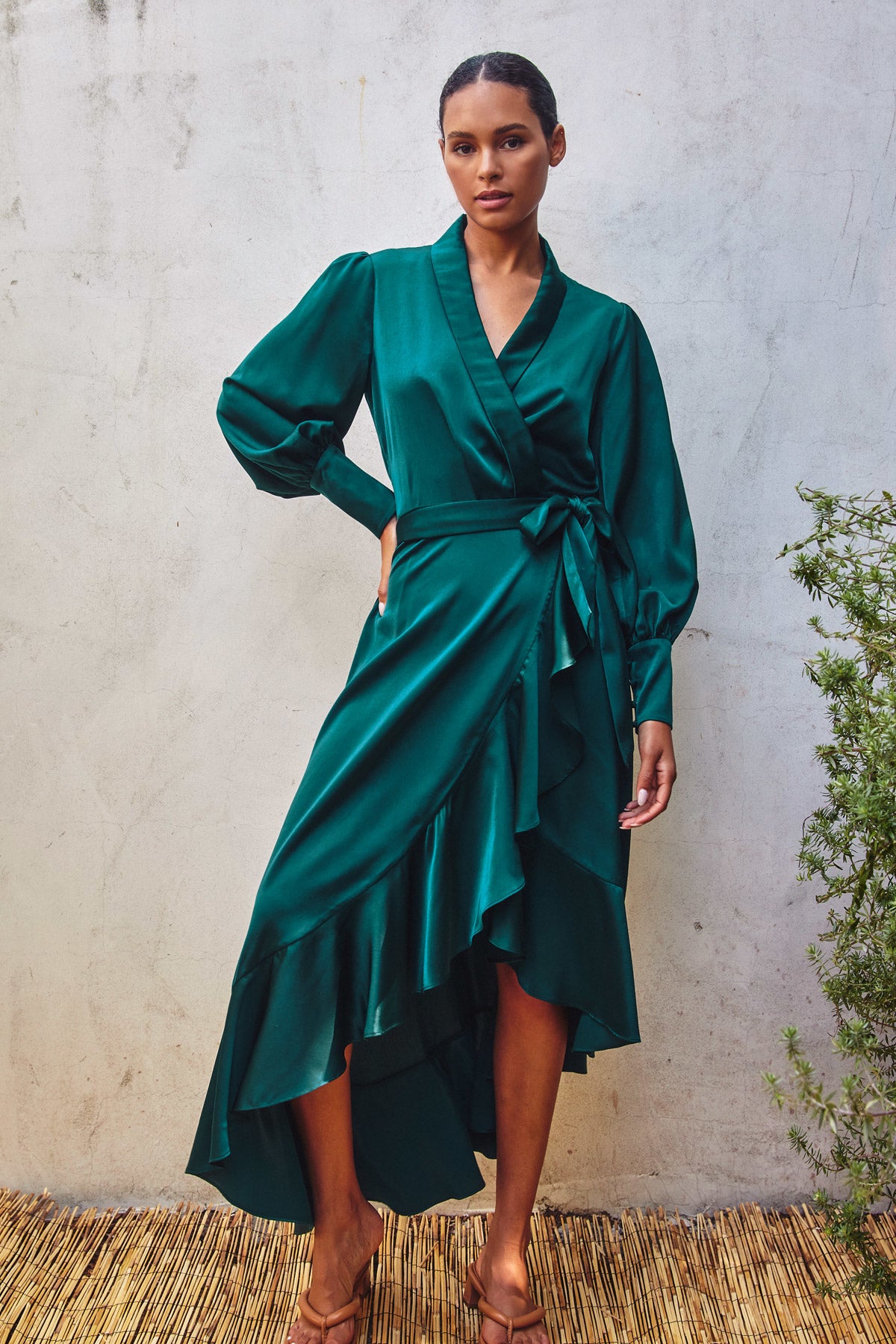 Model wearing a green satin holiday wrap dress with ruffles