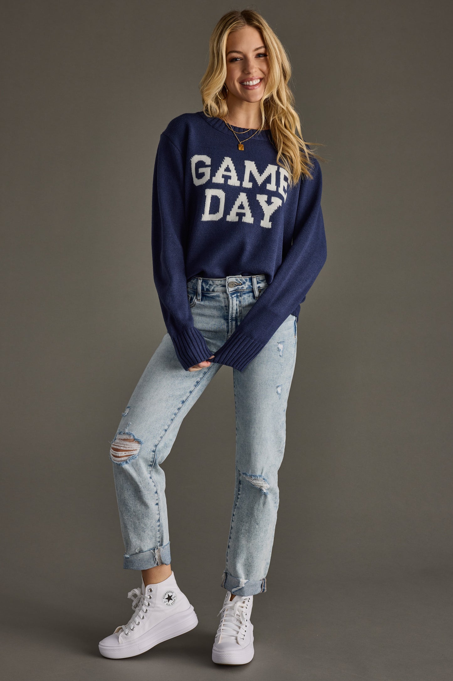 Woman wearing a navy 'GAME DAY' sweater with light blue jeans on a gray background