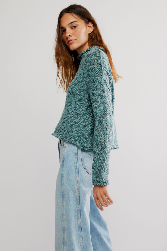 Woman wearing a green knitted sweater and light blue jeans on a white background